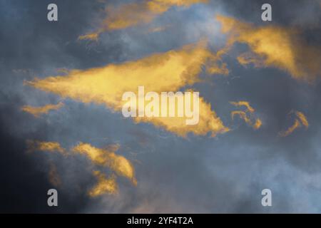 Nuages douillets dorés illuminés par des rayons en train de disparaître au coucher du soleil, cumulonimbus sombre flottant à travers le ciel bleu pour changer le temps de la saison. Incroyable vi Banque D'Images