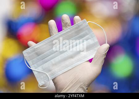 Le médecin tient le masque facial médical à la main dans des gants médicaux blancs sur fond de décorations de boules de Noël. Concept de confinement pour Noël et Happy New y Banque D'Images