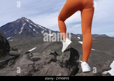 Vue arrière des jambes musclées des femmes portant un pantalon de yoga orange et des baskets blanches. Gros plan de la section basse d'un corps féminin athlétique pendant le fitness en plein air Banque D'Images