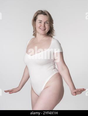 Portrait de la femme blonde adulte adulte mûre heureuse en costume de corps blanc posant en studio sur fond blanc. Mode de vie sain, concept de soins du corps. Smili Banque D'Images