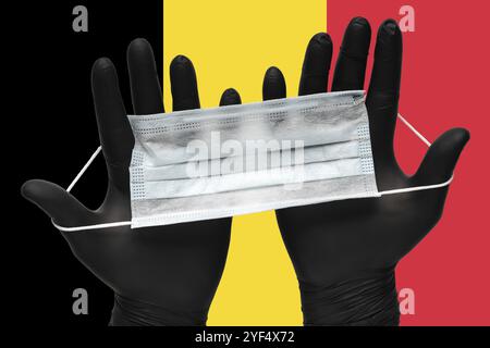 Le médecin tient le masque médical dans les mains en gants noirs sur les couleurs d'arrière-plan drapeau de Belgique. Concept assurance-pandémie coronavirus, quarantaine virale Banque D'Images