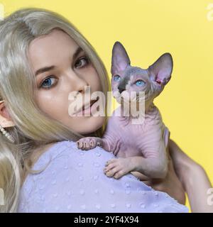 Portrait d'une jeune femme elfe cosplay tenant le chaton Sphinx dans les mains, souriant et regardant la caméra avec des yeux de différentes couleurs. Elf a une frise blonde Banque D'Images