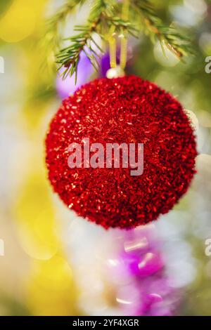 Vue rapprochée du ballon de Noël rouge vif et de la guirlande scintillante accrochée à la branche de l'arbre. Noël composition festive pour Bonne Année. Mise au point sélective Banque D'Images