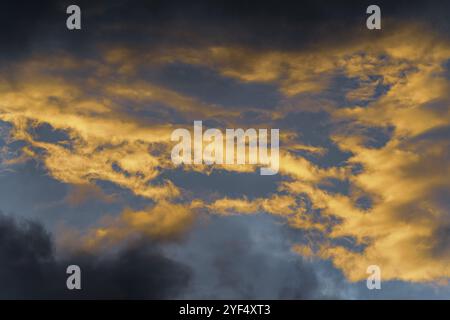 Nuages douillets d'or illuminés par des rayons en train de disparaître au coucher du soleil et des cumulonimbus sombres flottant à travers le ciel bleu ensoleillé pour changer le temps de la saison. Incroyable Banque D'Images