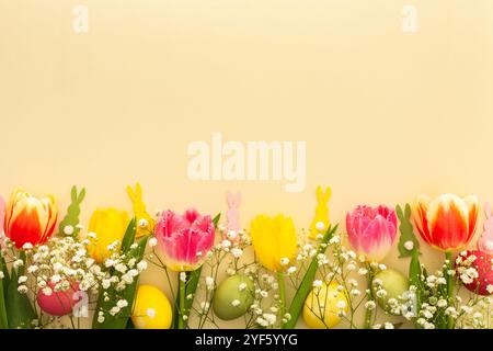 Fond de Pâques de printemps, oeufs de Pâques multicolores avec tulipes et gypsophila et lapins décoratifs sur fond jaune Banque D'Images