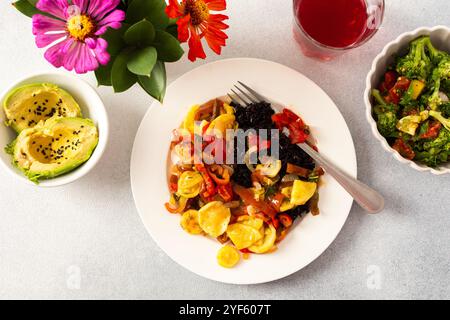 Une assiette nutritive et délicieuse avec riz noir aux légumes cuits, salade de tomates-brocolis-radis fraîches, avocat aux graines de sésame Banque D'Images