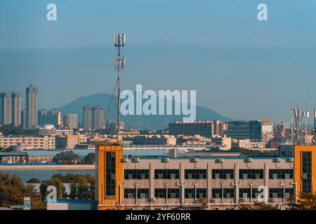 Horizon urbain avec des tours de télécommunications et des immeubles de bureaux contre une chaîne de montagnes lointaine sous un ciel bleu clair Banque D'Images