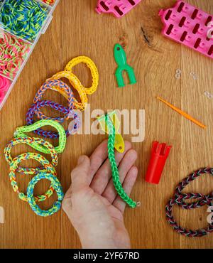 Main caucasienne tenant un travail en cours bracelet de métier à tisser, d'autres bracelets élastiques colorés et bracelet faisant des fournitures. Banque D'Images