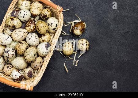 Oeufs de caille dans un panier en osier. Oeuf et plume sur la table. Fond noir. Pose à plat. Copier l'espace Banque D'Images