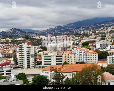 Une vue captivante comprend des gratte-ciel modernes combinés à des structures traditionnelles dispersées dans un paysage urbain vallonné, sous un ciel nuageux, montrant ur Banque D'Images