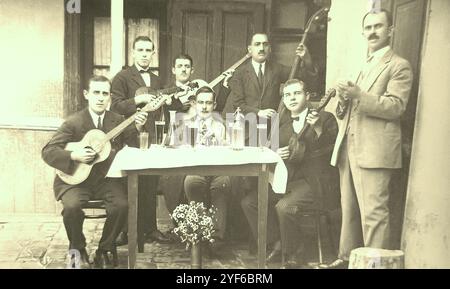 Cette photo vintage montre un homme aisé à une table de taverne, entouré d'un orchestre tambouritza et d'un propriétaire de taverne. Photo noir et blanc dans des tons sépia agréables. La photo a été prise par un photographe professionnel. La photo a été prise dans la ville de Novi Sad, Royaume de Yougoslavie, vers les années 1920-1930 Banque D'Images