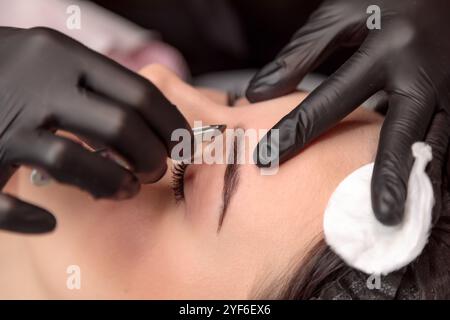 Esthéticienne cueillant les sourcils de la jeune femme avec des pinces à épiler dans le salon de beauté Banque D'Images