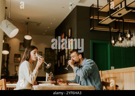 Deux personnes savourent leurs boissons à une table en bois, immergées dans une ambiance de restaurant détendue, tout en étant profondément dans la conversation et les rires. Banque D'Images