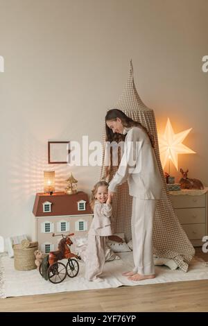 Mère et fille souriantes se tenant par la main et jouant dans une chambre avec un tipi de jeu et la maison de poupée Banque D'Images