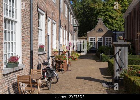 Béguinage médiéval dans le centre de Breda avec de petites maisons historiques décorées avec des plantes de jardin et une ancienne pompe à eau au premier plan. Banque D'Images