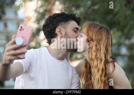 jeune couple aimant prenant un selfie avec téléphone portable embrassant dans le parc Banque D'Images