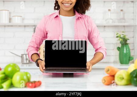 Une fille afro imreconnaissable tenant un ordinateur portable dans la cuisine Banque D'Images