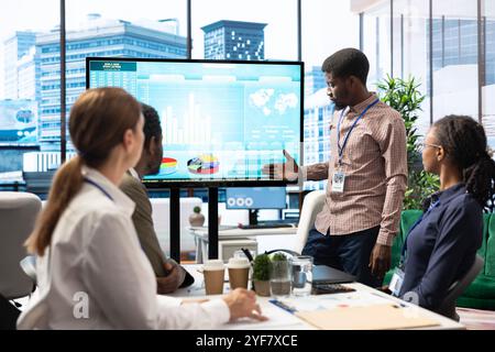 Employés d'une entreprise dans un espace de bureau haut de gamme collaborant sur des tâches de gestion de projet, en utilisant des outils numériques pour améliorer le flux de travail et la productivité. Examen des données volumineuses sur un tableau interactif. Banque D'Images