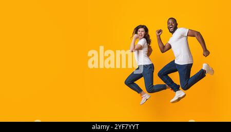 Couple interracial drôle sauter et courir dans les airs, fond jaune Banque D'Images