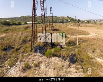 Vieux champ de prise de pompe de puits de pétrole rouillé à Albaina, drone aérien images dans la journée ensoleillée. Minuscules pompes à huile maison sur les Balkans Banque D'Images