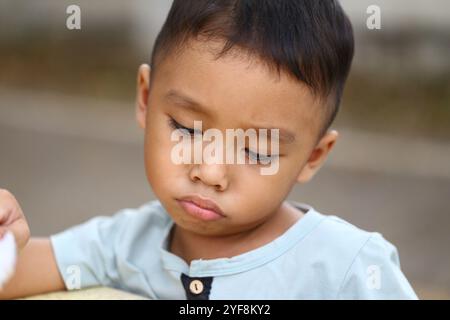 Ce portrait en gros plan capture un enfant pensif profondément dans la pensée, reflétant l’innocence et les émotions subtiles. La lumière douce améliore l'expression de l'enfant Banque D'Images