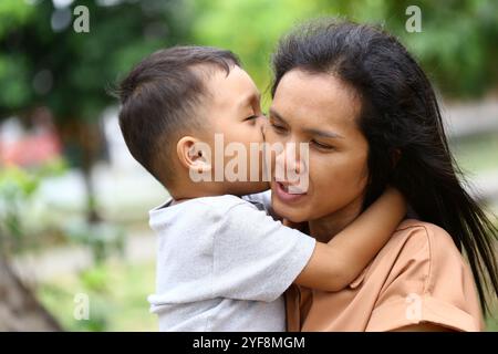 Une scène sincère d'une mère et d'un enfant partageant un baiser tendre dans un cadre extérieur, capturant la beauté de leur lien émotionnel étroit et de leur affection. Banque D'Images