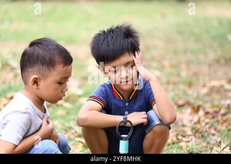 Deux jeunes garçons s’engagent dans un moment ludique en plein air, entourés par la nature. Leurs expressions dépeignent la curiosité et la joie, capturant l'essence de l'enfantho Banque D'Images