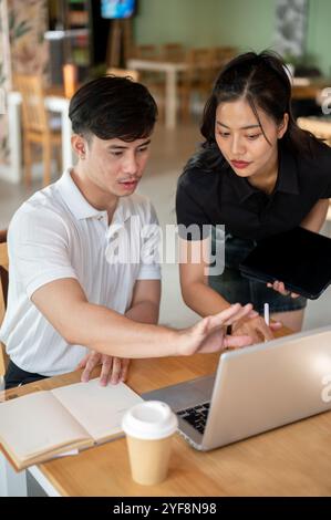 Deux collègues asiatiques concentrés, un homme et une femme, regardent un écran d'ordinateur portable, discutent de son contenu, font un brainstorming ensemble et partagent des idées Banque D'Images