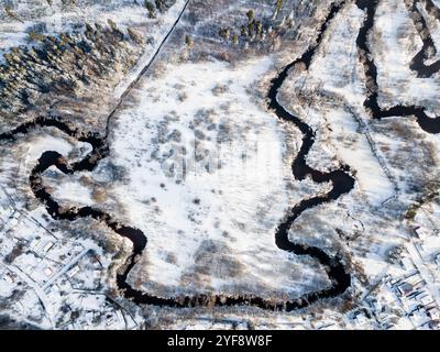 Vue aérienne sur la rivière d'hiver coulant à travers le champ avec l'arbre dessus. Tout est couvert de neige. Banque D'Images