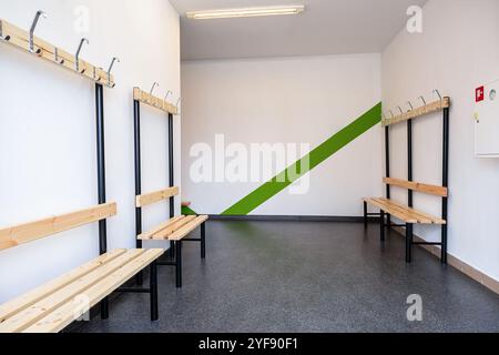 Vestiaire moderne avec murs rayés verts et blancs, bancs en bois et crochets à manteau Banque D'Images