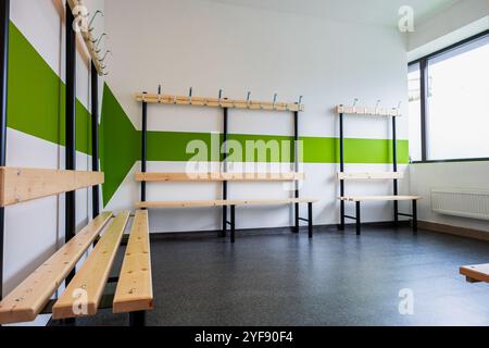 Vestiaire moderne avec murs rayés verts et blancs, bancs en bois et crochets à manteau Banque D'Images