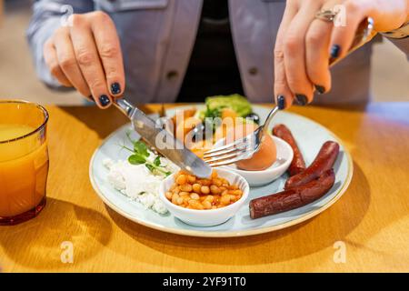 Femme mangeant le petit déjeuner anglais complet avec haricots, saucisses, œufs durs et jus d'orange Banque D'Images