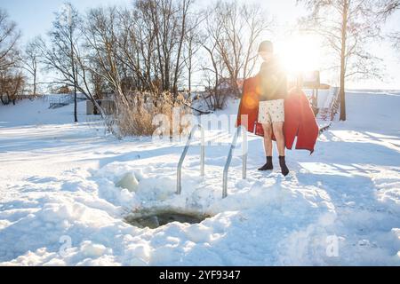 Nageur d'hiver enveloppé dans une serviette rouge après un plongeon rafraîchissant dans un trou de glace enneigé Banque D'Images