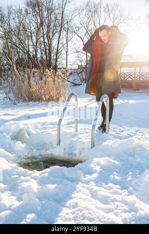 Nageur d'hiver enveloppé dans une serviette rouge après un plongeon rafraîchissant dans un trou de glace enneigé Banque D'Images