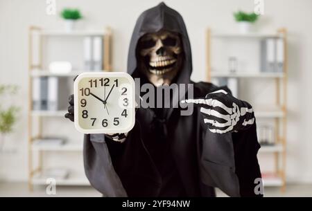 Homme d'affaires surmené dans le costume de mort d'Halloween pointant son doigt sur l'horloge dans le bureau. Banque D'Images