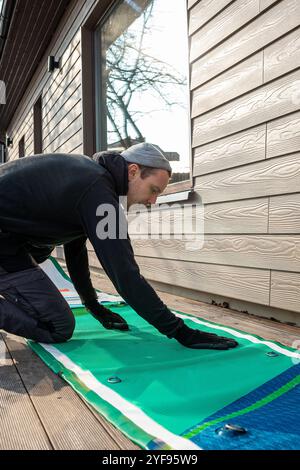 Homme pliant un stand-up paddleboard gonflable (SUP) sur une terrasse en bois à côté d'une maison moderne Banque D'Images