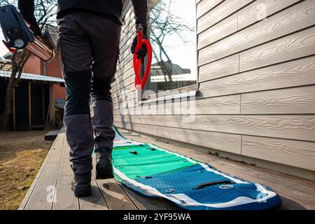 Homme avec une pagaie et gonflant une planche SUP sur une terrasse en bois près d'une maison Banque D'Images