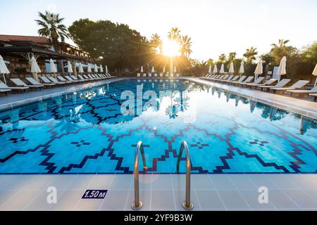 ambiance estivale relaxante dans un complexe luxueux avec chaises longues vides et parasols près d'une piscine immaculée entourée d'arbres luxuriants et bleu clair sk Banque D'Images