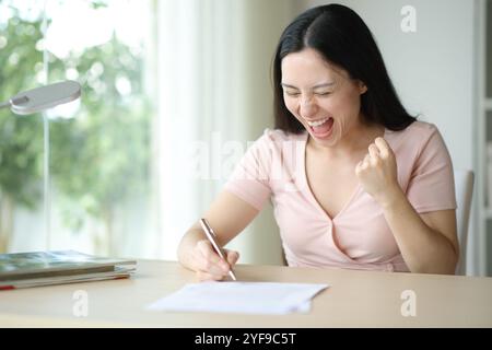 Femme asiatique excitée signant un contrat célébrant de bonnes politiques à la maison Banque D'Images