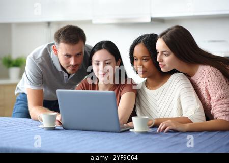 Quatre amis interraciaux sérieux utilisant un ordinateur portable ensemble dans la cuisine à la maison Banque D'Images