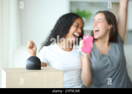 Amis interraciaux heureux chantant à la maison avec un haut-parleur intelligent jouant de la musique Banque D'Images