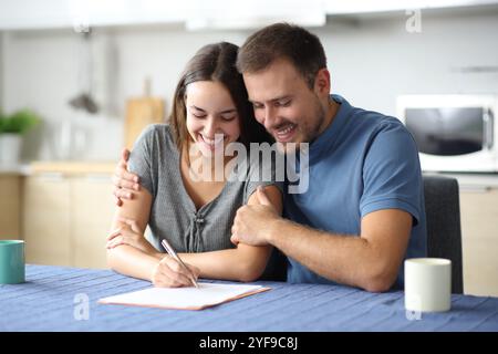 Couple heureux signant document papier dans la cuisine à la maison Banque D'Images