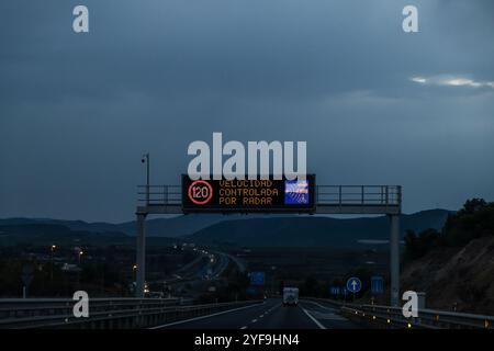 Photographie nocturne de la circulation sur une autoroute. Au premier plan, il y a un panneau lumineux élevé au-dessus de la route indiquant que la vitesse est contrôlée par Banque D'Images