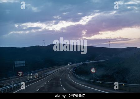 Beau coucher de soleil sur une autoroute en perspective courbe. Deux panneaux interdisent de conduire à plus de 120 km/h. Banque D'Images