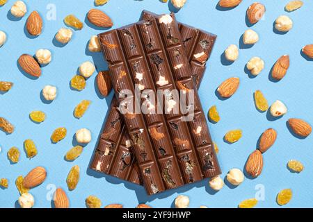 Barres de chocolat noisettes parmi les noix dispersées et les raisins secs sur un fond bleu. Banque D'Images