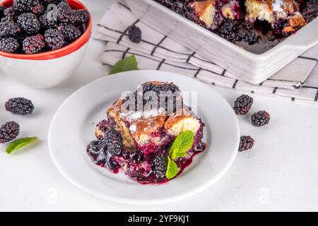 Tarte de cordonnier de mûrier maison sucrée, gâteau de cordonnier de baies d'été doux dans un plat de cuisson en émail et une assiette, sur un espace de copie de table de cuisine blanc Banque D'Images