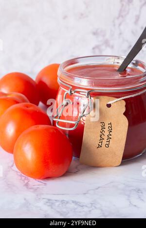 Tomate passata étiquetée dans un pot clip en verre avec des tomates et une cuillère. Sur un fond de marbre blanc Banque D'Images