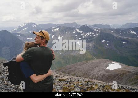 Jeune couple embrassant tout en randonnant sur la montagne contre le ciel nuageux Banque D'Images