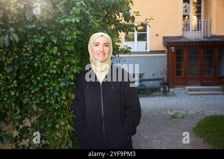 Portrait de belle femme souriante portant le hijab debout avec les mains dans les poches près des plantes Banque D'Images
