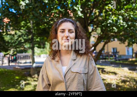 Portrait de belle jeune femme debout contre un arbre dans un parc public Banque D'Images